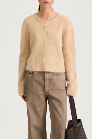 Model wearing a beige cardigan and brown pants with a white background