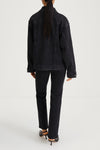 A model shown from the back wearing a black denim jacket and matching black jeans, paired with black high-heeled sandals, against a light gray studio background.