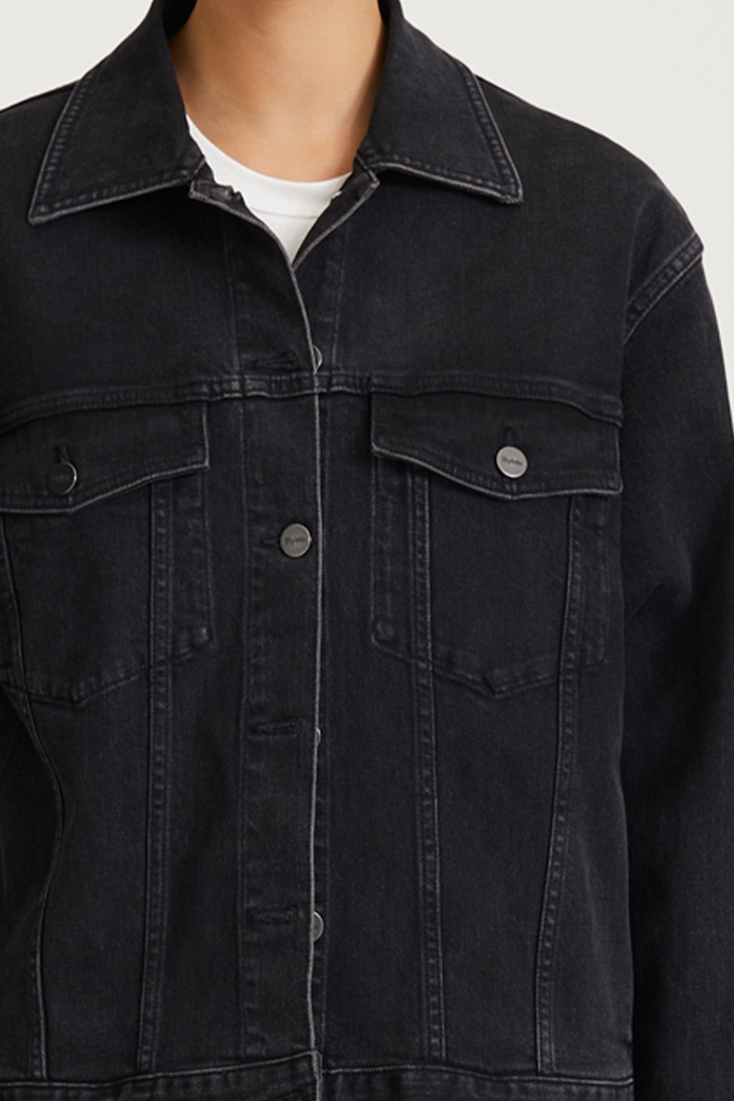 Close-up of a person wearing a dark washed denim jacket over a white t-shirt, showing the collar, front button placket, and chest pockets.