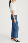 A side-profile view of a model wearing blue wide-leg cropped jeans, a white short-sleeve top, and black slingback heels against a clean white studio background.